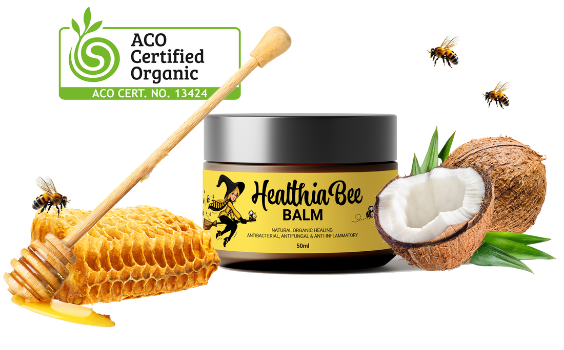 A jar of Healthia Bee balm with an illustration of a honeycomb with honey and a bee and a split coconut next to it. There is a label that reads ACO Certified Organic ACO Cert Number 13424.